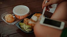 A hand holding a spoon near a meal of fried chicken, rice, and soup.